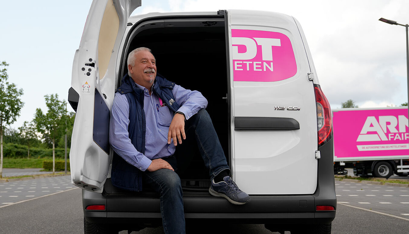 Arndt-Mitarbeiter sitzt lächelnd im Laderaum vom Transporter Citan 112 CDI | Autovermietung Arndt für Firmenkunden