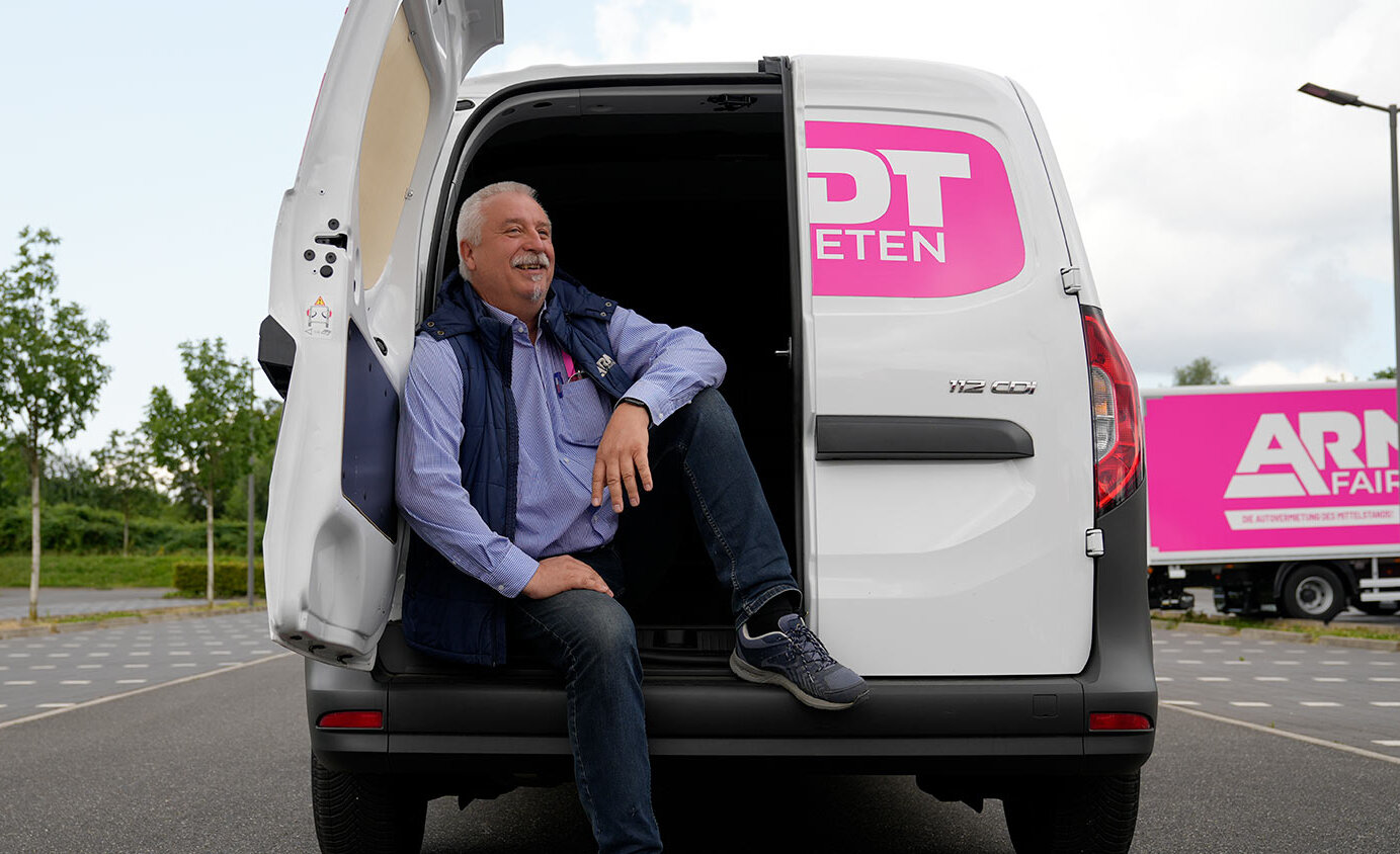 Arndt-Mitarbeiter sitzt lächelnd im Laderaum vom Transporter Citan 112 CDI | Autovermietung Arndt für Firmenkunden