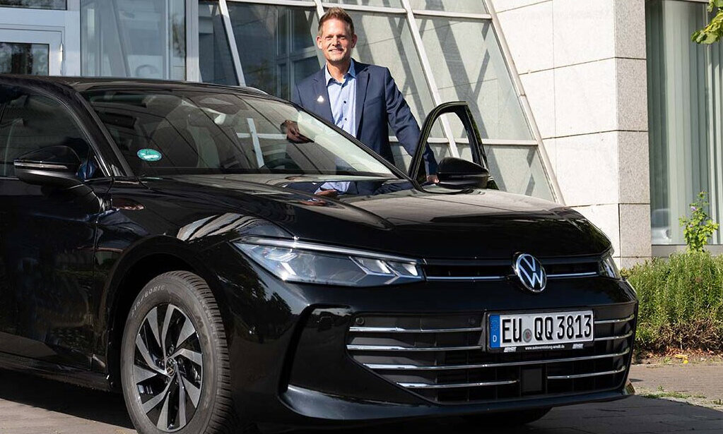 Ein Mann im blauen Sakko steht an der offenen Fahrertür eines schwarzen Volkswagen mit Arndt, geparkt vor einem modernen Bürogebäude | Autovermietung Arndt für Firmenkunden