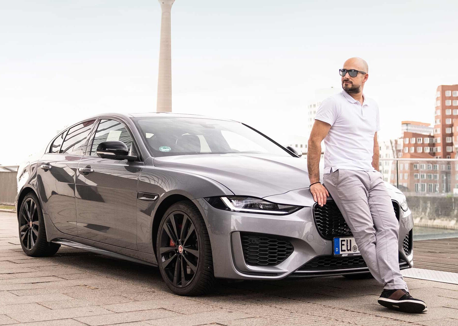 Eleganter Jaguar XE mit zufriedenem Kunden, stilvoller Auftritt vor urbaner Skyline am Medienhafen in Düsseldorf | Autovermietung Arndt für Firmenkunden